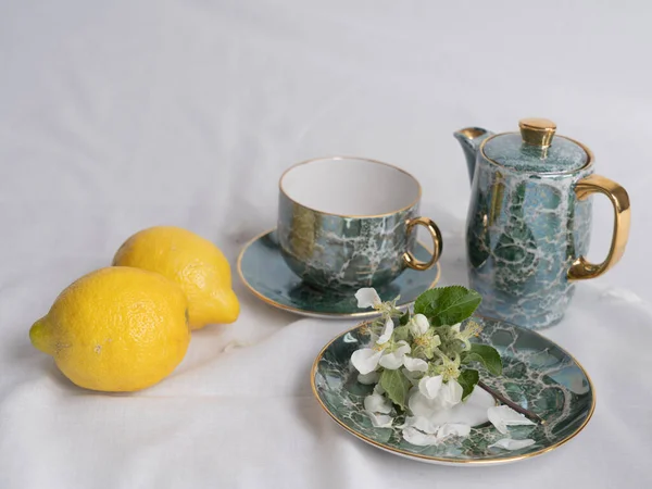 Still life in vintage style with a tea set, juicy lemons and apple blossoms on a white background. Time for tea. Space for text.