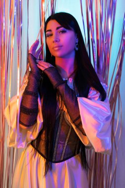 Siyah korseli, beyaz ipek elbiseli, uzun saçlı, güzel bir esmer. Arka planda pembe folyo perdesi var. Güzel stüdyo ışıkları. Kış fotoğraf çekimi.