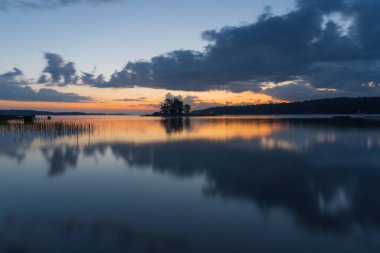Gün batımında gökyüzünün suda yansıması. Turuncu gün batımı ve kara bulutlar. Parlak dramatik gökyüzü. Finlandiya doğası. İskandinavya. Doğal arkaplan.