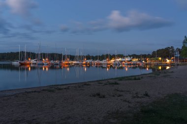 Nagu, Finlandiya - 12.06.2022: Birçok demirli yatla marinanın büyüleyici gece manzarası. İskelenin ışıkları resimli bir şekilde suya yansıyor..