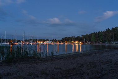 Nagu, Finlandiya - 12.06.2022: Birçok demirli yatla marinanın büyüleyici gece manzarası. İskelenin ışıkları resimli bir şekilde suya yansıyor..