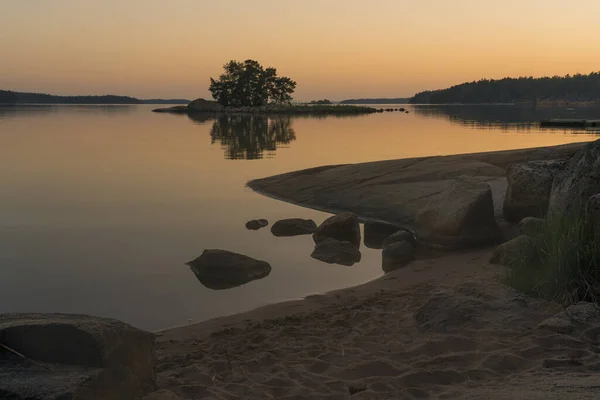 Nagu, Finland - 12.06.2022: the quiet shore of the bay after sunset. A line of trees and a small island on the horizon. Rocky coast in the foreground. Nature of Finland.