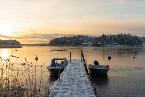 Soukka, Finland - 09.12.22: Winter sunset over the snow-covered islands in the bay. Frozen bay. Pier with boats in the foreground. Winter landscape. Scandinavia.