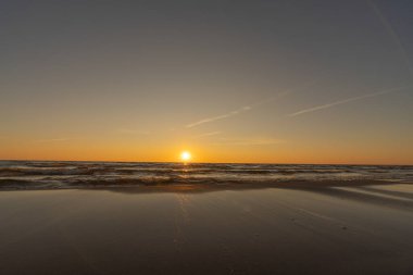 Sunset in a cloudless sky on the coast of the Gulf of Finland in Ust-Narva. The sky is clear, the waves gently roll on the sand. Estonia, Narva-Jyesuu. Natural background. Space for text.