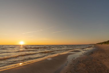 Sunset in a cloudless sky on the coast of the Gulf of Finland in Ust-Narva. The sky is clear, the waves gently roll on the sand. Estonia, Narva-Jyesuu. Natural background. Space for text.