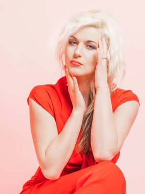 Kırmızı takım elbiseli güzel sarışın bir kadının portresi. Stüdyoda pembe bir arka planda otururken poz vermek.