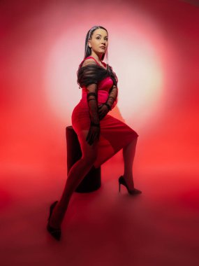 Pembe arka planda kırmızı elbiseli güzel bir esmerin portresi. Zarif siyah eldivenler giyiyor..