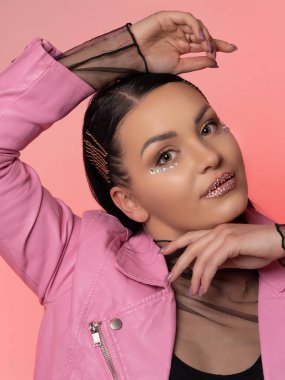 Pembe arka planda deri ceketli güzel bir esmerin portresi. Yakın plan. Yüzünde parlak bir parıltı var.