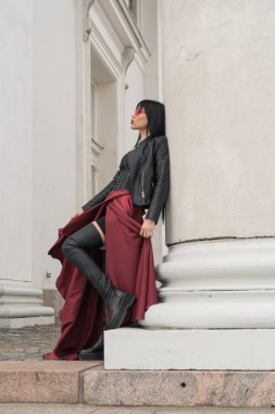 Uzun saçlı, mükemmel vücutlu, seksi bir kadın. Saten, uzun kırmızı etekli, deri ceketli. Şehirde eski sütunlarda poz vermek.