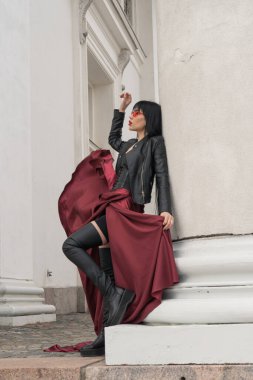 Uzun saçlı, mükemmel vücutlu, seksi bir kadın. Saten, uzun kırmızı etekli, deri ceketli. Şehirde eski sütunlarda poz vermek.