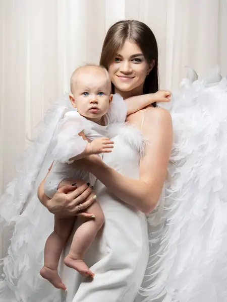 妈妈和女儿在天使的翅膀 演播室里的年轻女子和一岁大的婴儿照片 图库图片