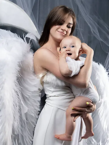 妈妈和女儿在天使的翅膀 演播室里的年轻女子和一岁大的婴儿照片 免版税图库照片