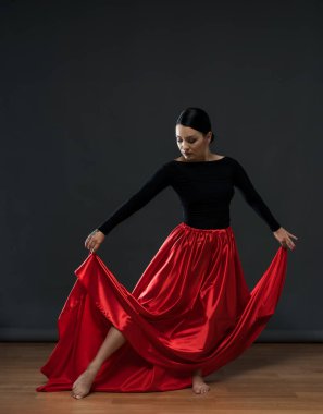 Parlak kırmızı etekli dansçı. Gri bir arka planda siyah elbiseli bir kadın dansçı..