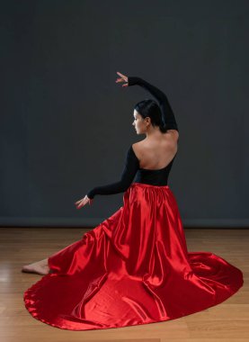 Parlak kırmızı etekli dansçı. Gri bir arka planda siyah elbiseli bir kadın dansçı..