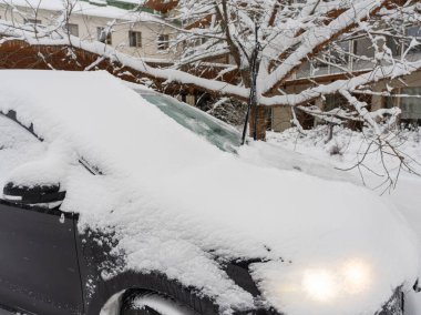 Karla kaplı bir arabanın ön camı buzlu ve ön farları buzlu tabakada parlayan bir bölümü. Olay yeri kıtır bir kış sabahını yakalıyor, yolculuktan önce bir araçtan kar temizlemenin soğukluğunu anımsatıyor..