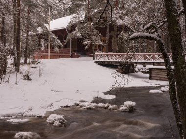 A secluded winter landscape with a rushing stream or waterfall amidst snowy banks. A vintage bridge is visible. The atmosphere of harmony and silence of the forests winter nature, cozy tranquility, like a Christmas day. clipart