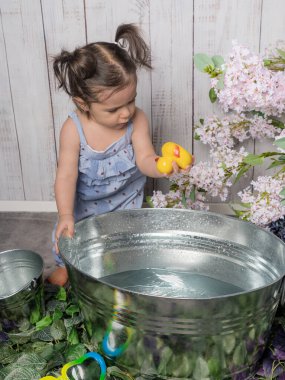 Viktorya dönemi romantizmi tarzında lüks bir stüdyo fotoğrafı. Zarif bir elbise içindeki çekici bir kadın şehvetli çiçeklerle bezenmiş bir iç mekanda antika mobilyalar, retro ışıklandırma ve eski mankenler gibi antika elementlerle poz veriyor. 