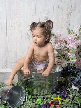 A little girl playing in a copper bathtub or bathing basin with a retro design, surrounded by rubber bath toys. A playful and cozy scene evoking childhood memories. clipart