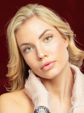 Büyüleyici gözleri olan, zarif beyaz bir elbise giymiş, çarpıcı sarışın bir kadının yakın planda çekilmiş portresi. Yumuşak ışıklandırma onun narin özelliklerini ön plana çıkarıyor, zamansız ve sofistike bir görünüm yaratıyor..