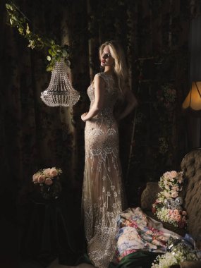 An elegant blonde in a luxurious embroidered evening dress poses in a vintage interior surrounded by flowers. A glamorous look, sophistication, aristocratic charm, and a romantic atmosphere. clipart