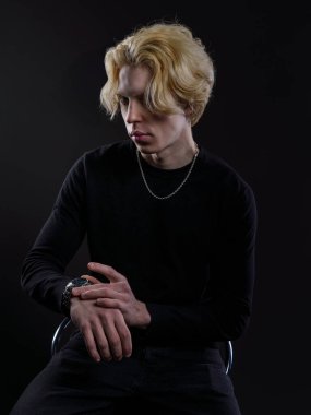 Siyah elbiseli, dalgalı sarı saçlı, koyu bir arka planı olan genç bir adamın portresi. Yüzünde ciddi bir ifade ve bakışları çok yoğun. Dramatik ışıklandırma yüz hatlarını ve saçlarını ön plana çıkarıyor.