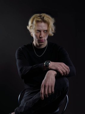 Siyah elbiseli, dalgalı sarı saçlı, koyu bir arka planı olan genç bir adamın portresi. Yüzünde ciddi bir ifade ve bakışları çok yoğun. Dramatik ışıklandırma yüz hatlarını ve saçlarını ön plana çıkarıyor.