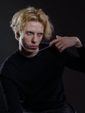 Siyah elbiseli, dalgalı sarı saçlı, koyu bir arka planı olan genç bir adamın portresi. Yüzünde ciddi bir ifade ve bakışları çok yoğun. Dramatik ışıklandırma yüz hatlarını ve saçlarını ön plana çıkarıyor.