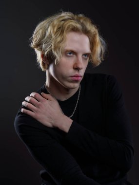 Siyah elbiseli, dalgalı sarı saçlı, koyu bir arka planı olan genç bir adamın portresi. Yüzünde ciddi bir ifade ve bakışları çok yoğun. Dramatik ışıklandırma yüz hatlarını ve saçlarını ön plana çıkarıyor.