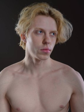 Siyah arka planda dalgalı sarı saçlı genç bir adamın sanatsal portresi. Çıplak omuzlar, el göğüste. Düşünceli bakış, melankolik ifade. Yumuşak ışıklandırma yüz özelliklerini vurgular