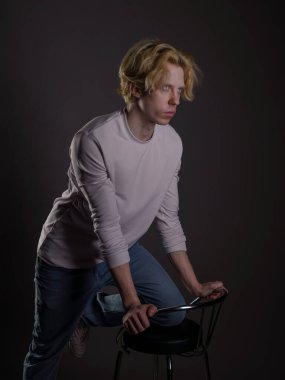 Siyah arka planda dalgalı sarı saçlı beyaz elbiseli genç bir adamın portresi. Yüzünde ciddi bir ifade ve bakışları çok yoğun. Atmosferik ışıklandırma yüz hatlarını ve saçı vurguluyor 