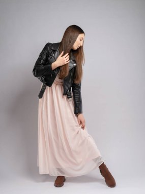 Model testinde genç bir kadın, tam boy. Hareket, dalgalı pembe elbise, deri ceketli kontrast. Tarafsız arkaplan, pembe balonlar neşe ve hafiflik ekler