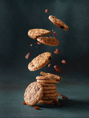 Kuru üzümlü lezzetli yulaflı kurabiyeler yığının içine düşüyor. Koyu bir arka planda yulaf ezmeli kurabiyeler