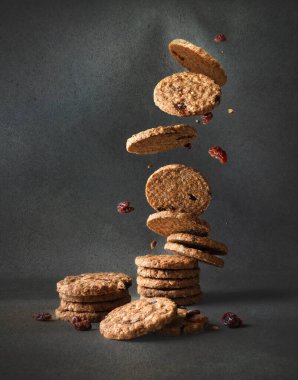 Üzümlü yulaflı kurabiyeler gri arka planda bir yığın üzerine düşüyor.