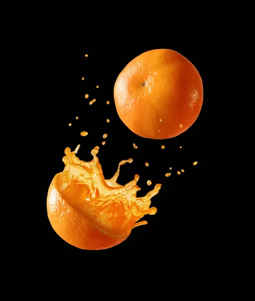 Whole and a half orange with splashes of juice on a black background