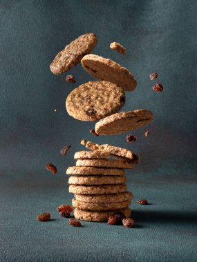 Kuru üzümlü yulaflı kurabiyeler arka planda bir yığının içine düşüyor.