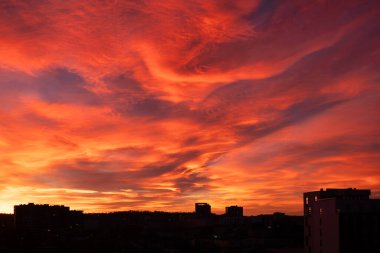 Gün batımında ev siluetleriyle nefes kesici, renkli bir gökyüzü. Alacakaranlıkta gün batımında mavi, mor ve turuncu güneş ışığı