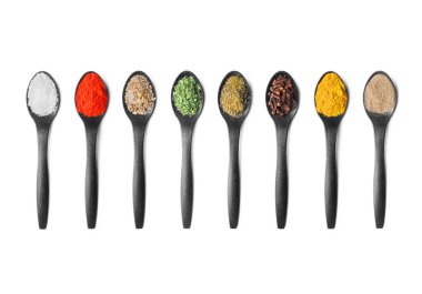 Beyaz arka planda düzgünce düzenlenmiş çeşitli renklerde baharat ve baharatlarla dolu bir sıra siyah kaşık.