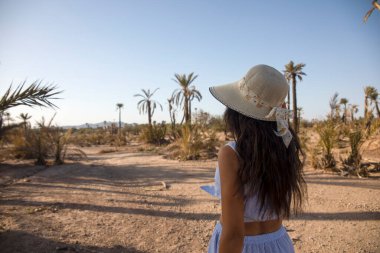 Şapkalı turist çöl manzarasının ve palmiye ağaçlarının tadını çıkarıyor. Palmiye bahçesindeki Marakeş şehrini sunan bu yer Fas 'ta turistler tarafından çok ziyaret ediliyor..