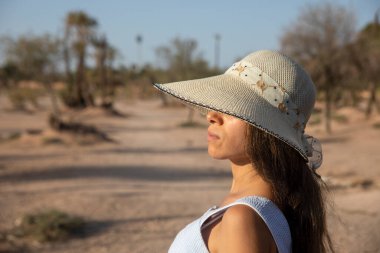 Şapkalı seksi turist, çöl manzarasında oturmaktan ve palmiye ağaçlarından faydalanıyor. Bu yer Fas 'ta turistler tarafından çok ziyaret ediliyor..