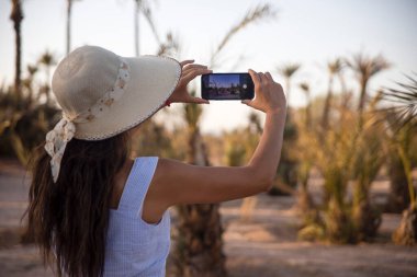 Marakeş palmiyesinin tadını çıkaran turist, akıllı telefonuyla fotoğraf çekerken şapkasıyla kendini güneşten koruyor. Fas 'taki bu çöl evi turistler tarafından çok ziyaret ediliyor..