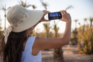 Marakeş 'in palmiye bahçesinin akıllı telefonuyla fotoğraf çeken seksi bir turist. Bu çöl, Fas' ın en güzel ve ziyaretçilerinden biri..