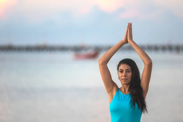 Concentrated woman doing yoga and meditating on the shores of the riviera mayan beach at sunrise in a relaxing, warm and beautiful environment at the magic hour of the day that is ideal for this sport