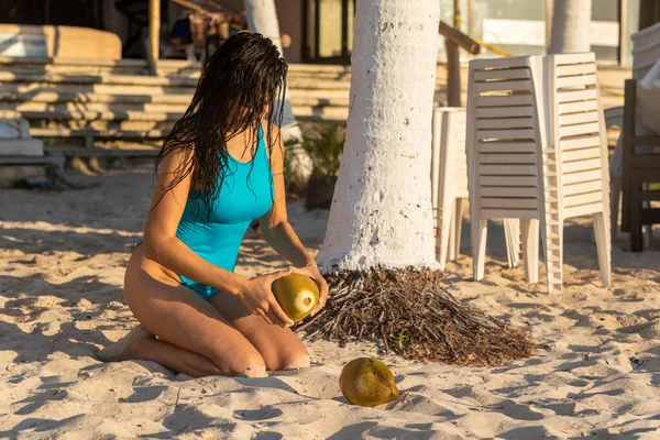 Picture of sexy woman with two coconuts in her hand that she will open to drink on a beach in the Mexican Mayan Riviera, ideal place to sunbathe, enjoy the sea water and the sand of the beach.