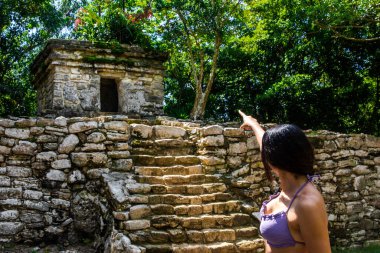 Genç turist, Meksika 'nın Maya Rivierası' ndaki Xcaret Park 'taki Maya mimarisinin harabelerine işaret ediyor. İspanyol öncesi bir kültür geride pek çok kültür bıraktı..