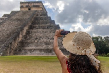 Meksika 'nın Chichen Itza şehrindeki Kukulcan piramidinin önünde duran şapkalı seksi turist kız. Seyahat konsepti. Meksika, Yucatan 'daki Maya piramitleri ve harabeleri.