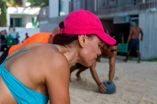 stock image Sexy woman with a group of athletes doing exercises with medicine ball on the beach sand, strengthening biceps, triceps and pectorals. Fitness concept.