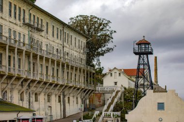 Amerika Birleşik Devletleri 'nin San Francisco, Kaliforniya körfezindeki Alcatraz Adası' ndaki federal hapishanenin kışlası ve metal gözetleme kulesi. Bulutlu bir gökyüzünün altında gözetleme. Hapishane kavramı.