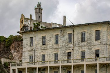 Amerika Birleşik Devletleri 'nin San Francisco, Kaliforniya, ABD' deki Alcatraz Adası federal hapishanesinin kışlası ve deniz feneri. Bulutlu bir gökyüzünün altında gözetleme. Hapishane kavramı