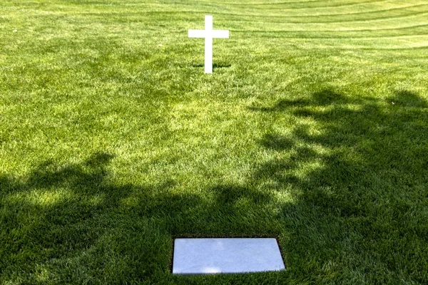Cross and white marble tomb on a grassy lawn at Arlington National Cemetery, a military cemetery in Washington DC, the capital of the USA.