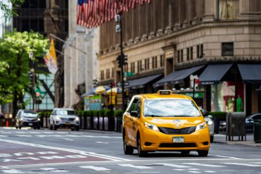 New York, ABD; 4 Haziran 2023: Manhattan 'daki Beşinci Cadde' de Amerikan bayraklarının altından geçen sarı bir taksi, New York 'taki Büyük Elma' nın merkezinde (ABD).